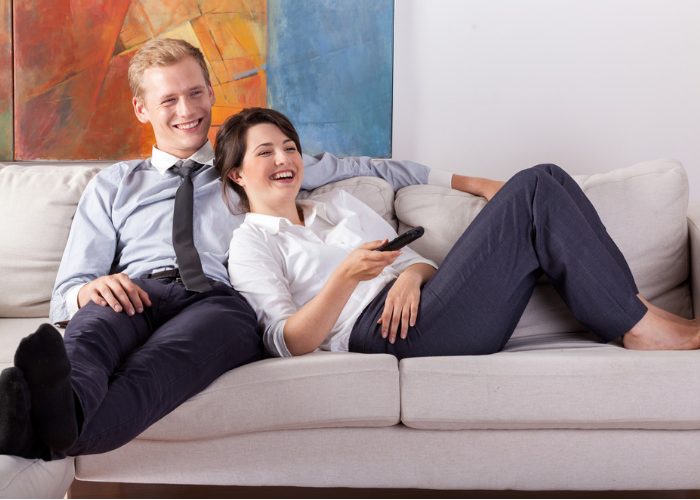 A young heterosexual couple relaxing on the couch after work watching TV