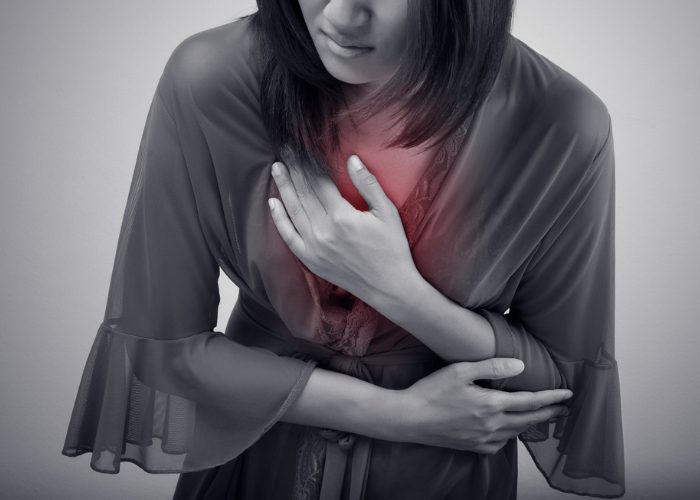 Greyscale image of a woman slightly hunched over holding a pain in her chest