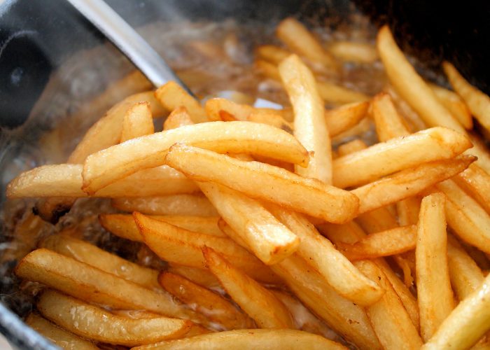 Close up of hot steaming deep fried french fries coming out of the deep fryer