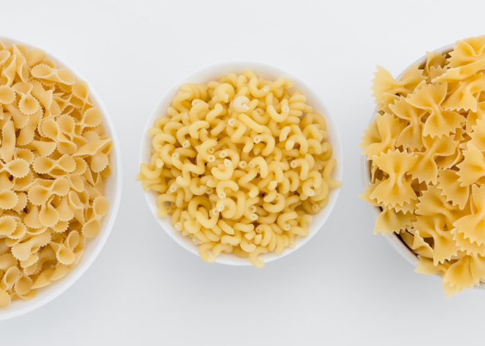 Top down image of three white bowls with different pastas in them on a white table