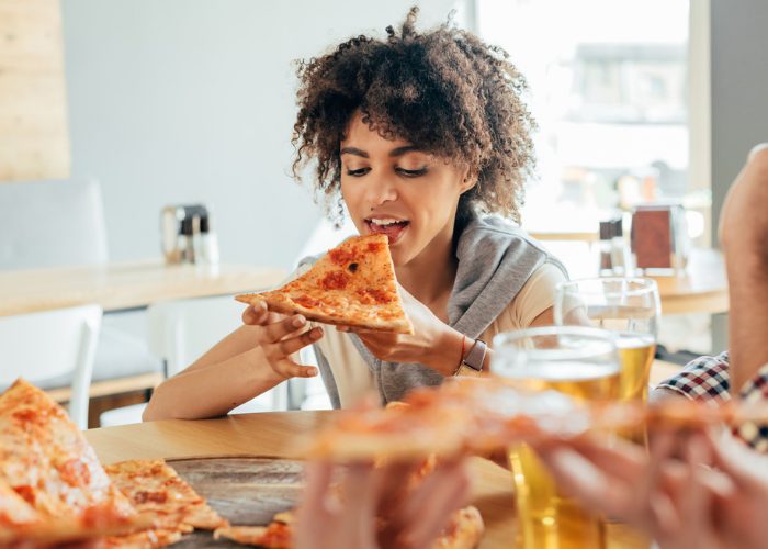 Woman with curly hair eating a slice of pizza in a restaurant