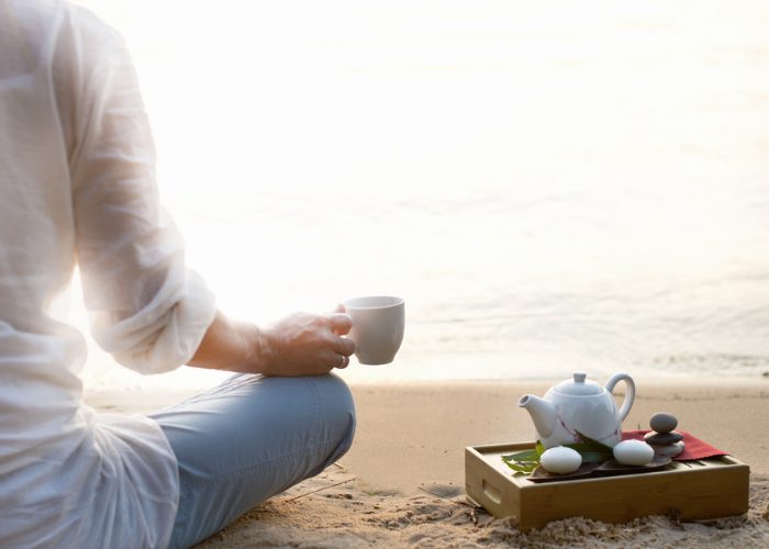 Woman sat on the beach relaxing with a pot of tea and looking out to sea