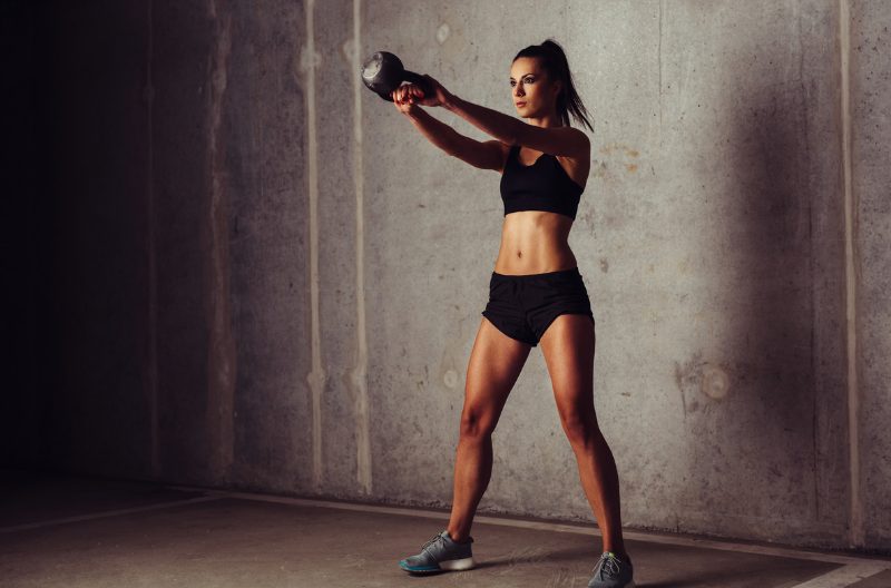 Fit woman with toned abs and legs swinging a kettlebell for strength training