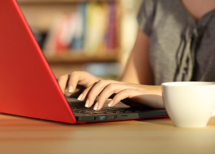 Woman using a red laptop with a coffee cup beside her