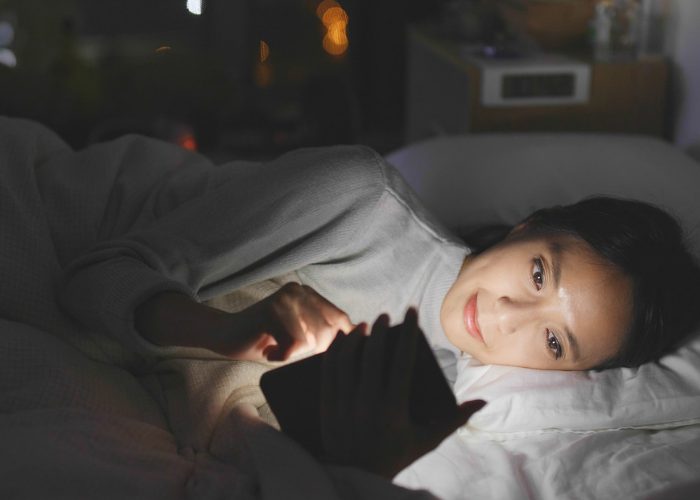 Woman lying on her side in bed at night and using her smartphone with a bright blue light