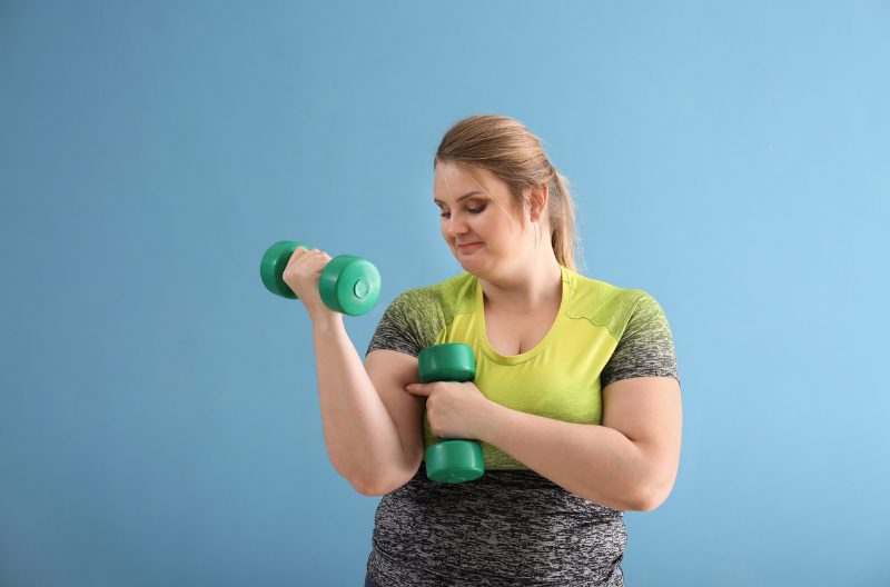 Plus size woman in exercise gear doing dumbbell curls and body positive workout