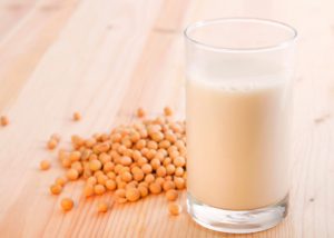 A glass of non-dairy soy milk on a wooden table with a pile of soy beans next to it