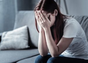 Depressed woman on her couch with her face buried in her hands 