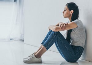 Depressed woman sitting alone on her floor backed against a wall