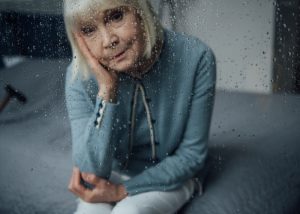 Depressed elderly woman staring through a glass window with raindrops on it