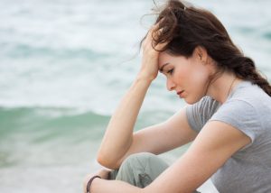 Sad woman by the beach holding her head in her hands 