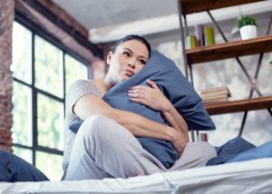 Depressed woman holding onto her pillow in bed