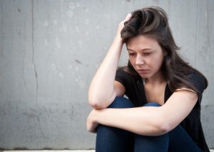 Young, depressed woman sitting with her back against the wall