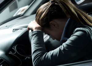 Tired and depressed woman in a formal work jacket laying her head on the dashboard of her car