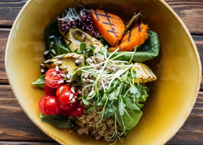 A healthy salad of sprouts, grains, and vegetables, in a yellow bowl on a wooden table