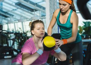 A female personal trainer coaching her female trainee through a workout at the gym
