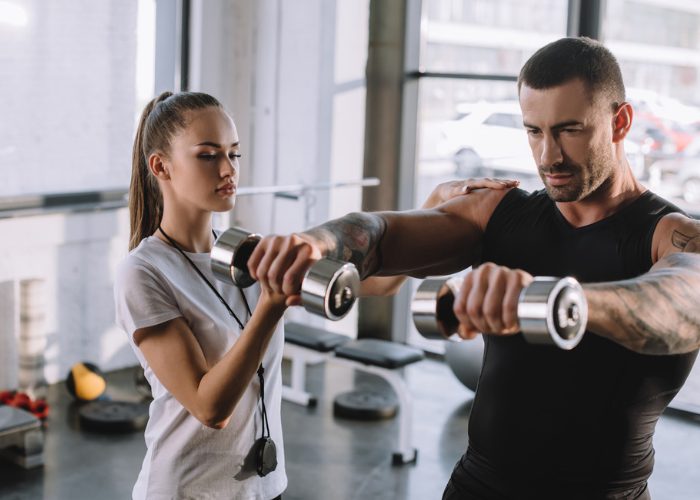 Female personal trainer coaching a male client at the gym using weights