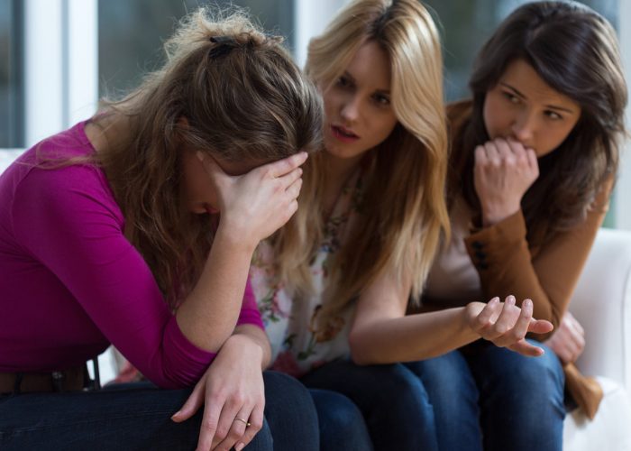 Two young female friends sitting on a couch listening to and comforting their depressed friend as they talk