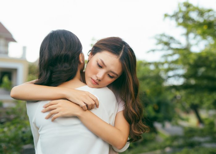 Two women hugging with trees in the background