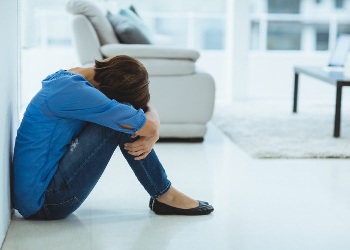 Depressed woman sitting on her living room floor with her head on her knees