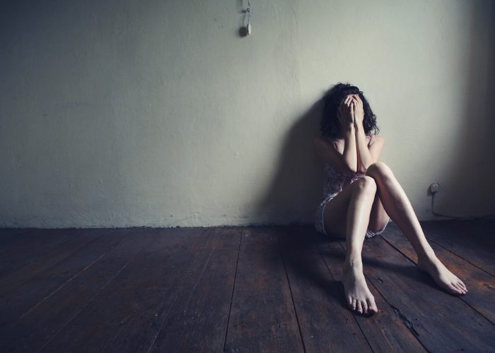 Depressed woman sitting on the floor in a dark room with her back against the wall