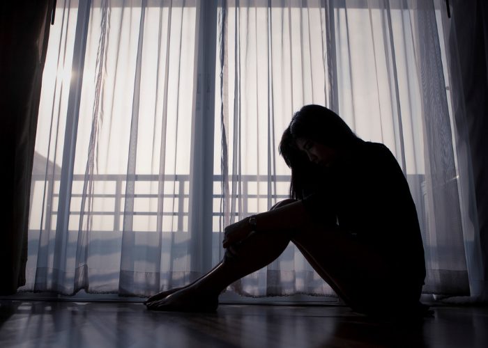 Dark silhouette of a sad woman sitting on the floor of a dark living room