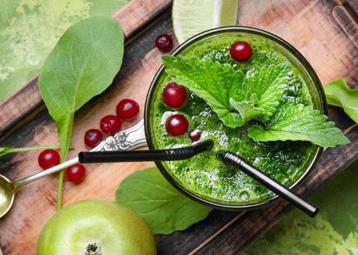 Top down view of a glass of spinach and cranberry smoothie topped with mint leaves and whole cranberries