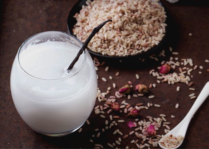 A glass of non-dairy rice milk with a straw, and rice scattered around it