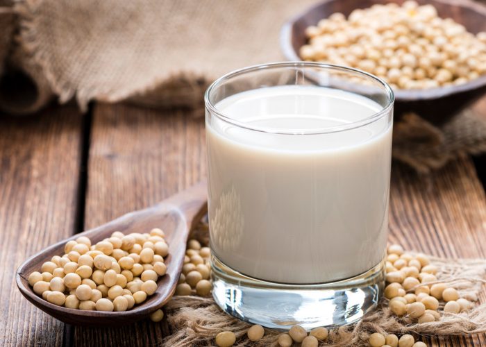 A glass of non-dairy soy milk with a wooden spoonful of soybeans next to it on a wooden table