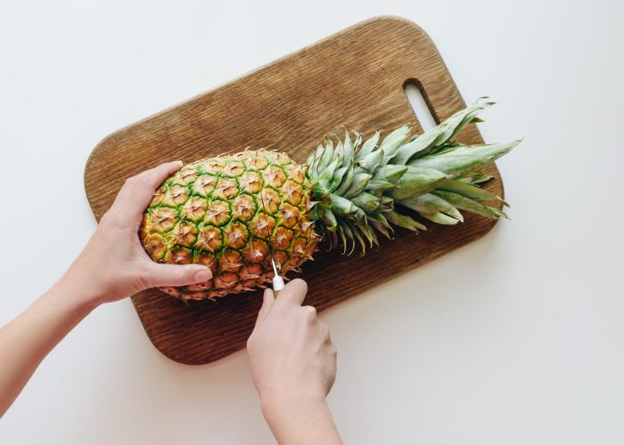 Woman cutting a whole pineapple on a wooden chopping board