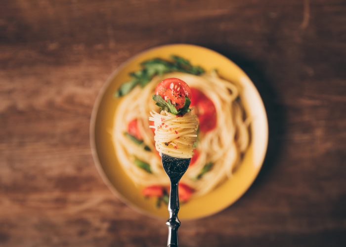 Top down image of fork with a swirl of spaghetti, cherry tomato, and basil on top of a plate of paste