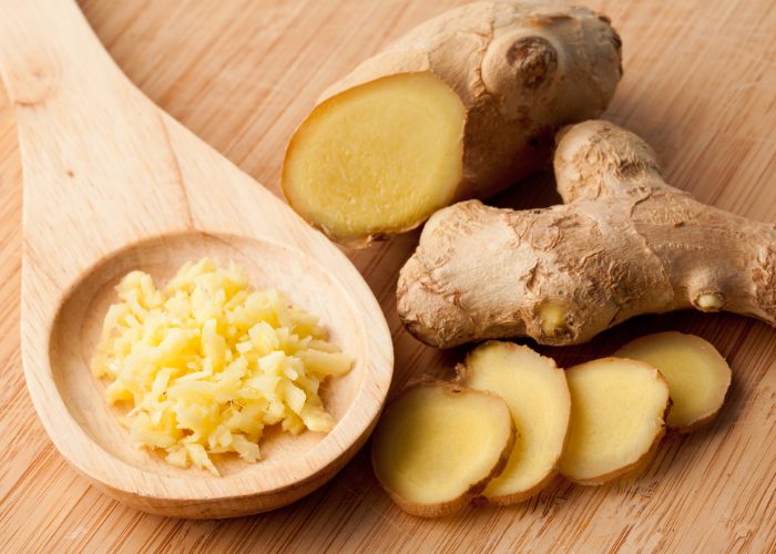A wooden spoonful of chopped ginger, sliced ginger, and whole ginger on a wooden table to represent one of the strongest natural antibiotics