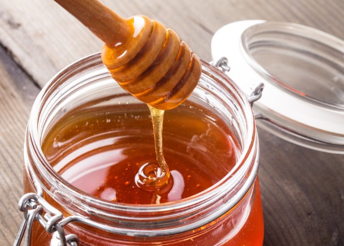 Close up of honey dipper with dripping honey over a honey jar