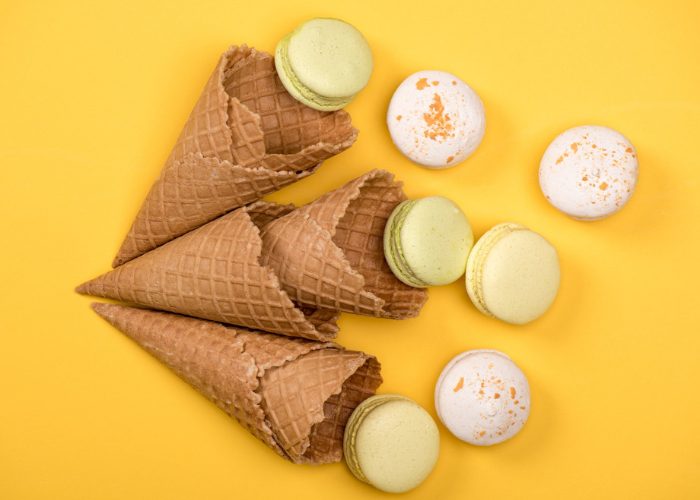 Empty ice cream wafer cones and light colored macaroons laid against a yellow background