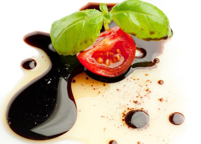 Close up of piece of cherry tomato and basil leaf on balsamic vinegar and olive oil