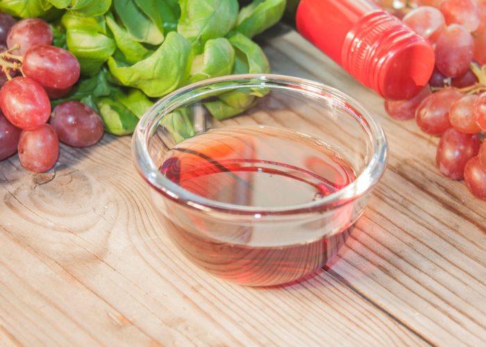 Small clear dish of red wine vinegar with red grapes in the background