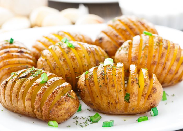Roasted accordion potatoes on a white dish sprinkled with parsley