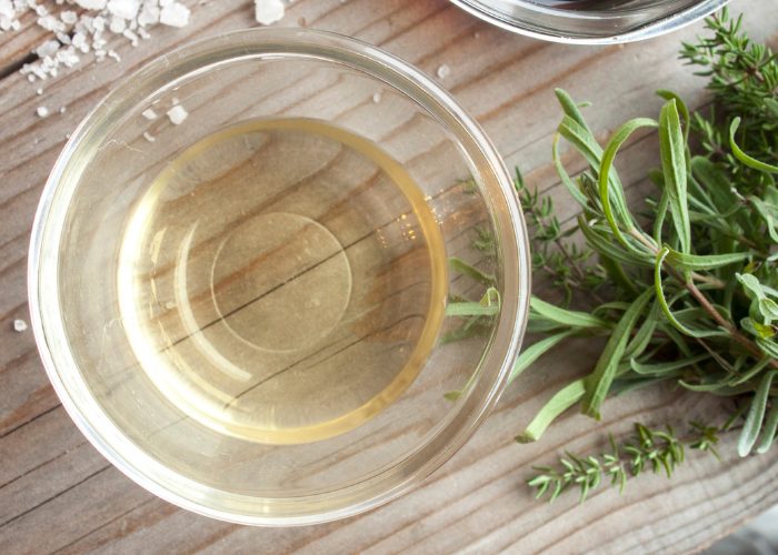 Small glass dish with white distilled vinegar in it next to herbs and salt 