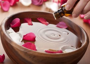 Woman adding aromatherapy oil to a bowl of water with rose petals