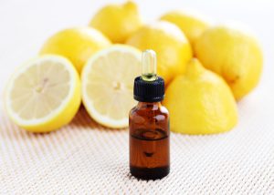 A bottle of lemon aromatherapy oil with a pile of fresh lemons in the background