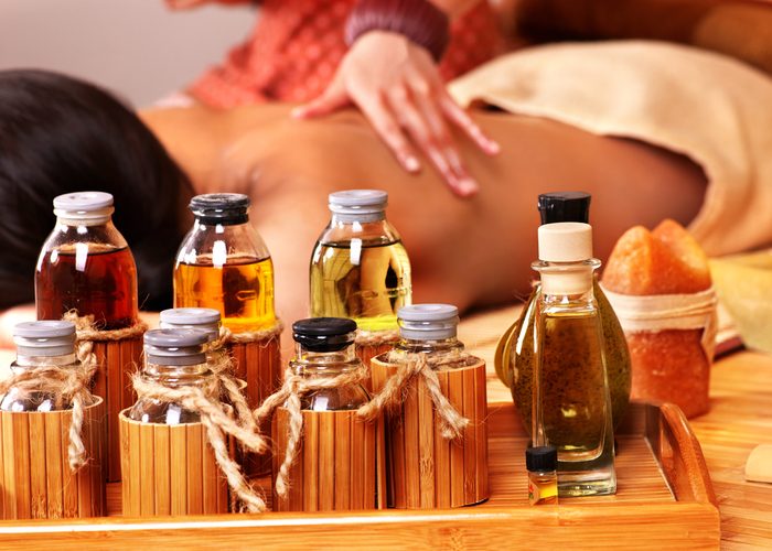 Bottles of aromatherapy oils in a massage studio with a woman getting a massage with them in the background.