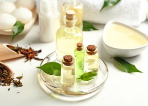 A plate featuring tea tree aromatherapy oil bottles of different sizes with aromatherapy creams and candles in the background 
