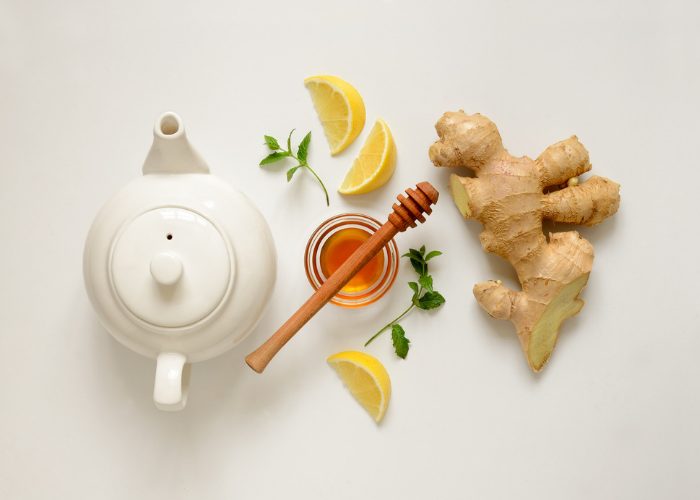 A flat lay featuring a tea pot, honey pot, slices of lemon, and ginger. 