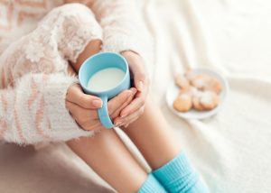 A woman sitting on her bed holding a cup of warm milk