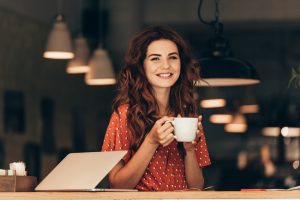 Woman smiling and drinking coffee at a cafe as she works 