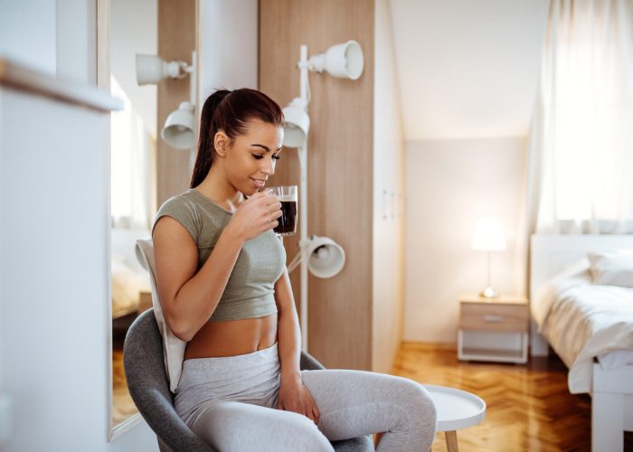 Woman sitting in her bedroom post-workout drinking a cup of detox tea