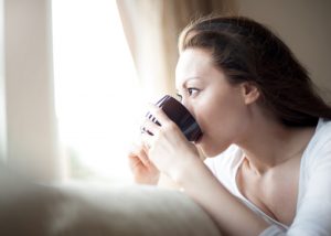 Woman staring out the window drinking a cup of detox tea