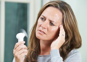 Woman with a headache and hot flashes using a small handheld electric fan