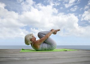 Elderly woman doing yoga outdoors on a wooden deck