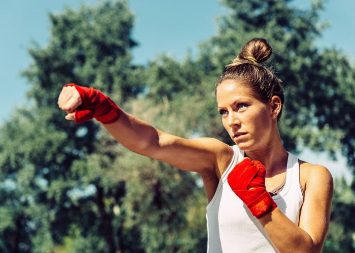 Woman in a park with wrapped fists practicing Tae Bo kickboxing